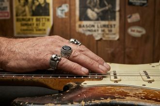 Main de guitariste portant des bagues rock en argent avec motifs tête de mort sur le manche d'une guitare électrique usée