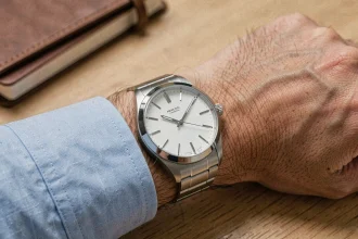 Montre analogique AM-PM au cadran blanc portée au poignet d'un homme en chemise bleue sur un bureau en bois, gros plan réaliste