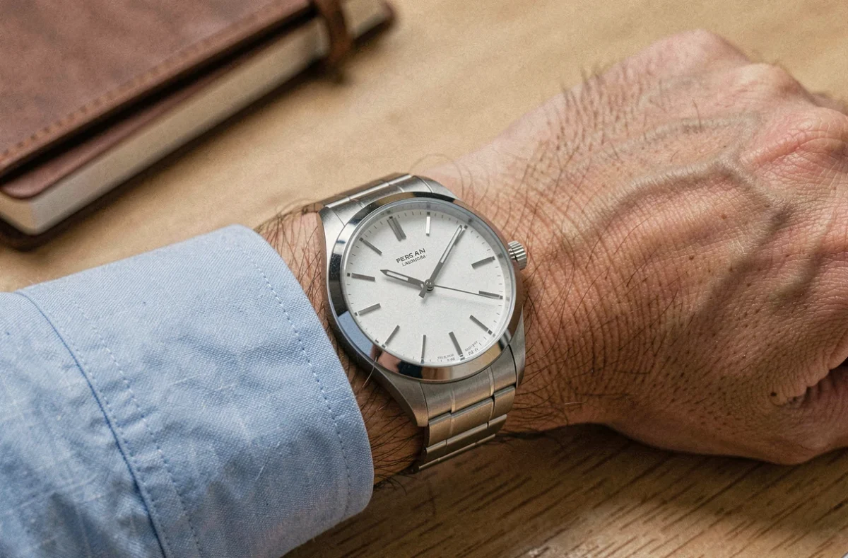 Montre analogique AM-PM au cadran blanc portée au poignet d'un homme en chemise bleue sur un bureau en bois, gros plan réaliste
